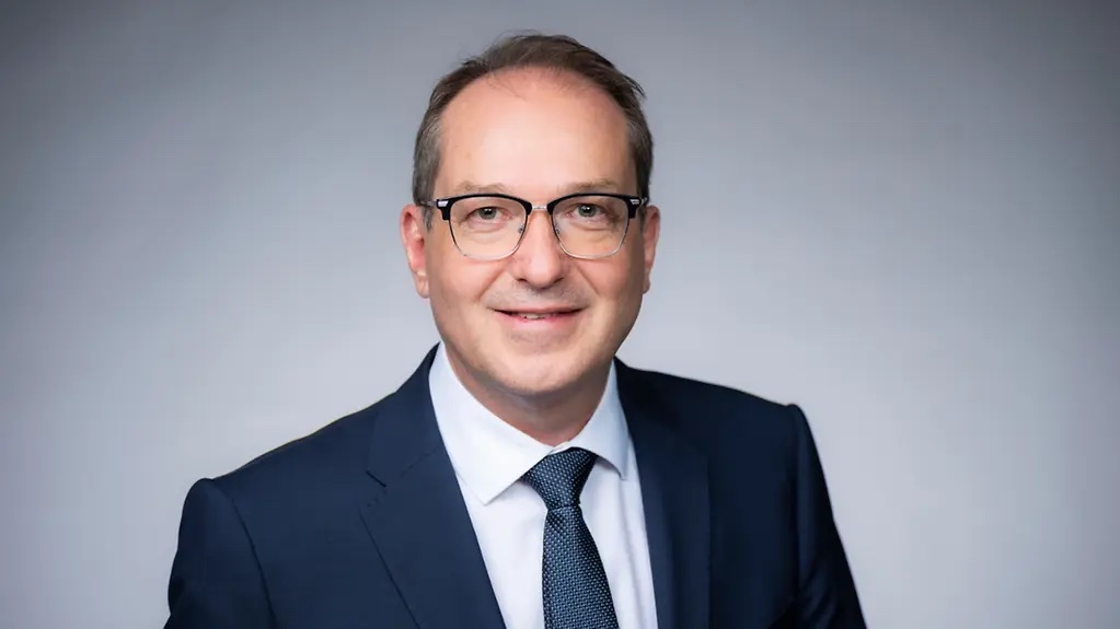Studio portrait of Alexander Dobrindt smiling, wearing glasses, a dark blue suit and a patterned tie