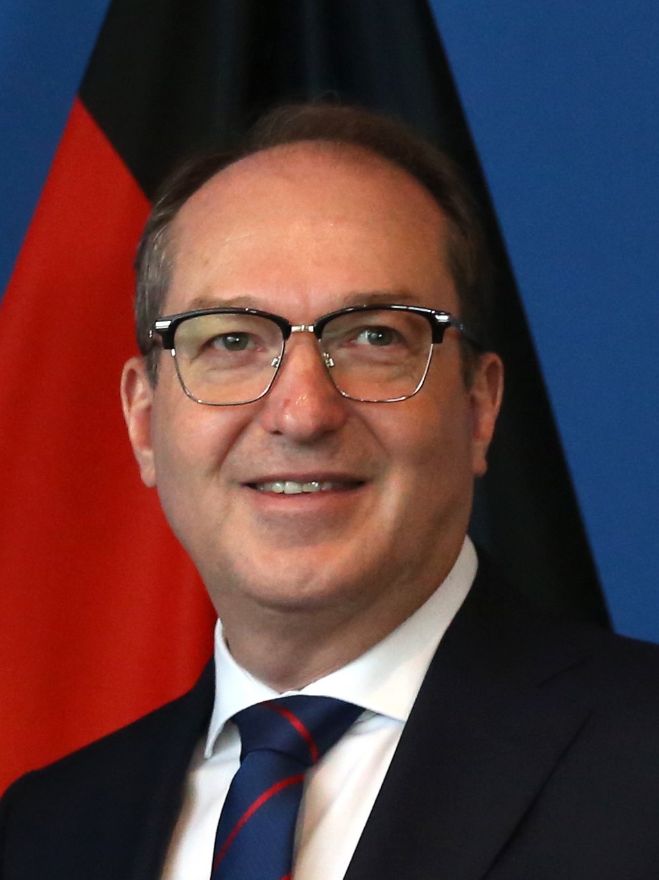 Official portrait of Alexander Dobrindt smiling in front of the German flag