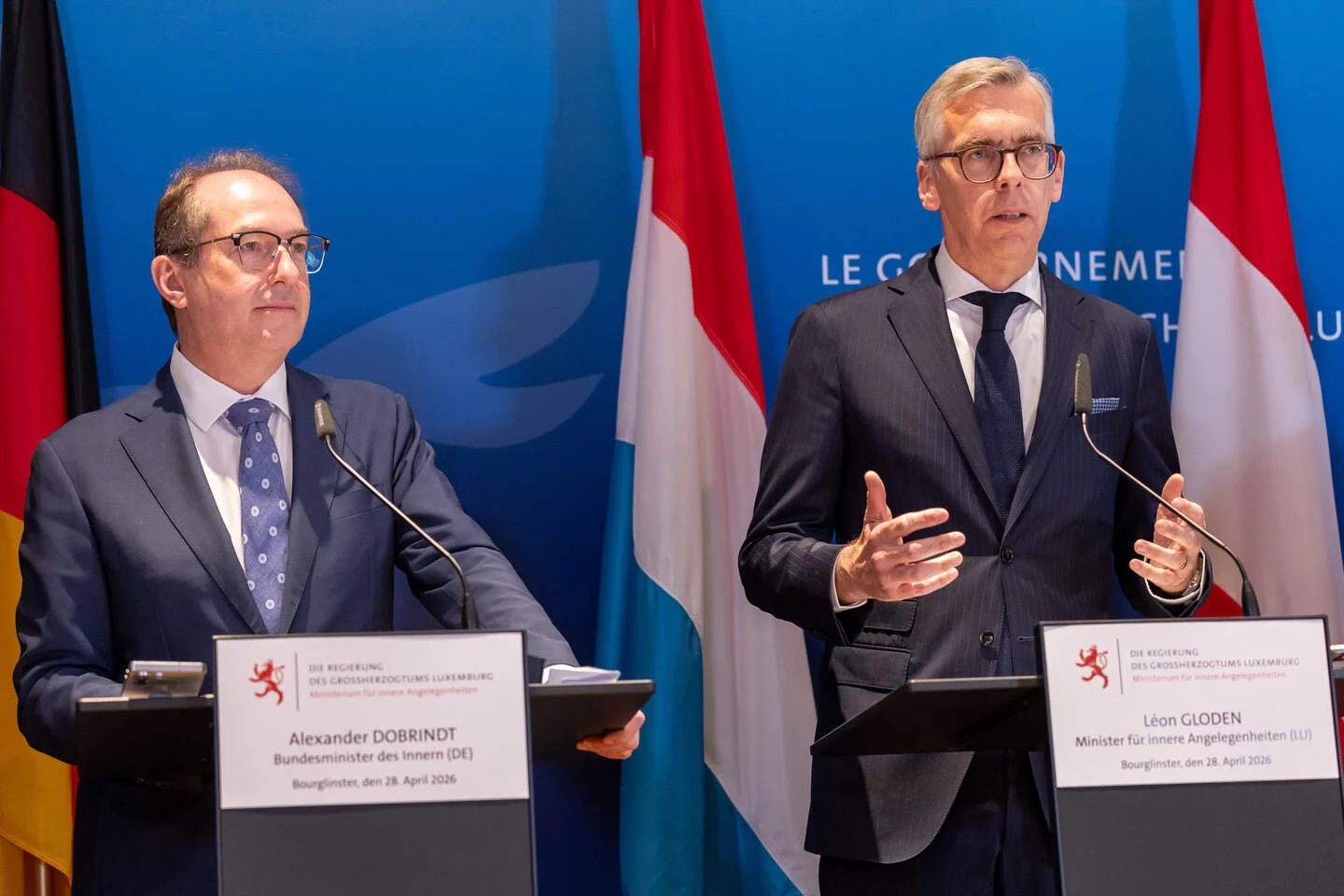 Alexander Dobrindt listening at a lectern beside Luxembourg’s interior minister Léon Gloden, who is speaking, in front of German and Luxembourg flags