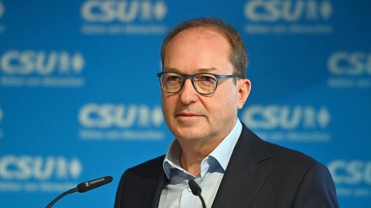 Alexander Dobrindt speaking at a microphone in front of a blue CSU backdrop